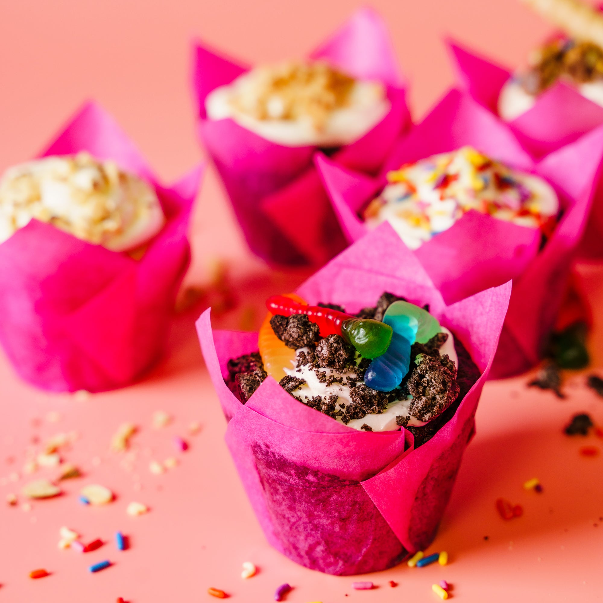 Cupcakes in pink wrappers on a pink background with colorful sprinkles.